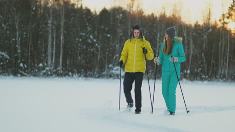 In-the-winter-forest-at-sunset-loving-couple-skiing-and-look-around-at-the-beauty-of-nature-and-attractions-in-slow-motion.
